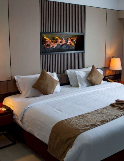 A cozy hotel room with a large bed, decorative pillows, bedside lamps, and a modern wall feature, creating a welcoming atmosphere.