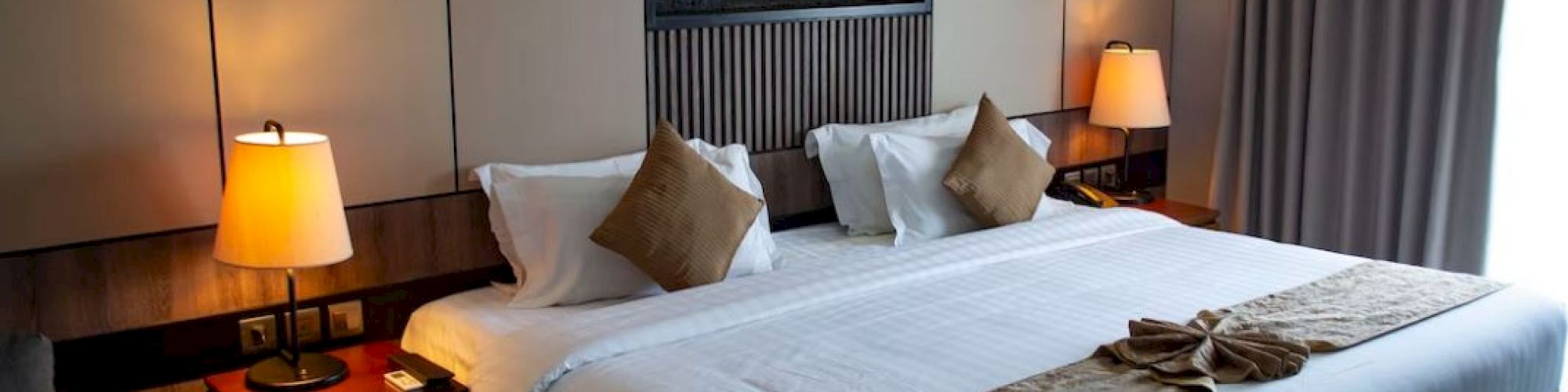 A cozy hotel room featuring a large bed with cushions, modern lamps, and a decorative piece above the headboard.