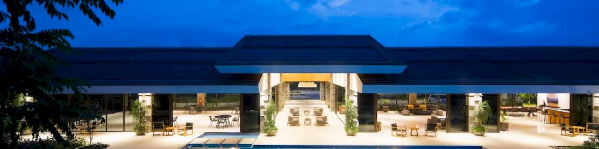 A luxurious poolside view at dusk with a spacious, well-lit modern building surrounded by a serene, inviting atmosphere.