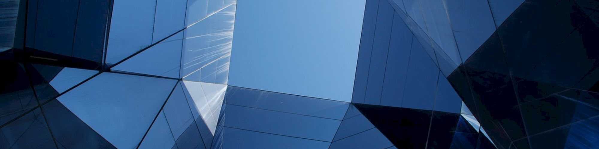 This image shows an architectural view looking up at glass-paneled buildings with a clear sky visible in the center.