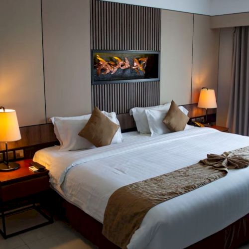 A hotel room with a neatly made bed, two bedside lamps, decorative pillows, and a modern design featuring warm tones and curtains.