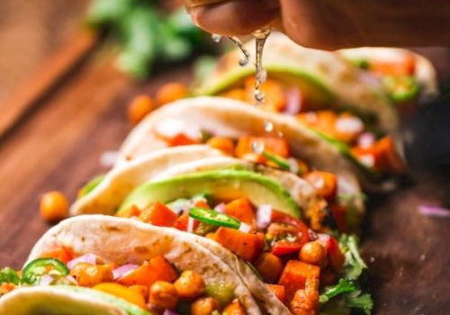 A hand squeezes lime over tacos filled with chickpeas, vegetables, and avocado on a wooden board.