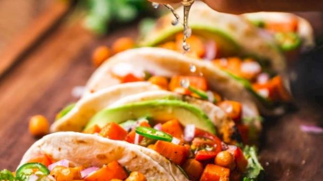 A hand squeezes lime over tacos filled with chickpeas, vegetables, and avocado on a wooden board.