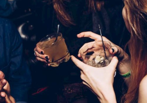People are socializing, holding drinks, and laughing in what appears to be a lively, indoor setting.