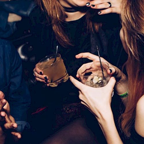 People are socializing, holding drinks, and laughing in what appears to be a lively, indoor setting.