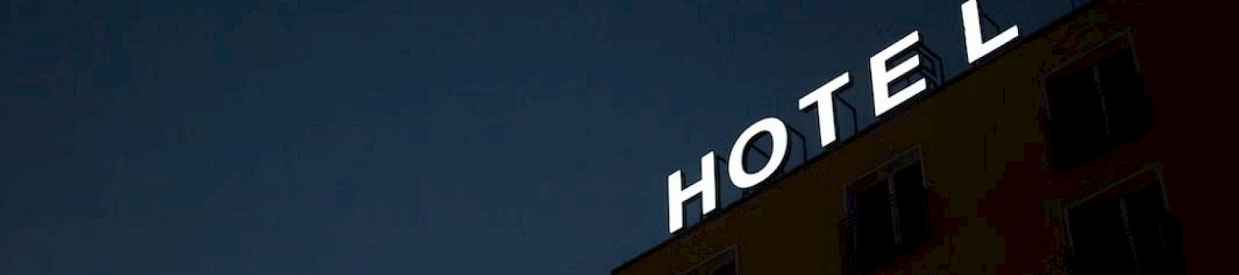 A building with the word "HOTEL" in bright lights, missing the letter "E" against a dark evening sky.