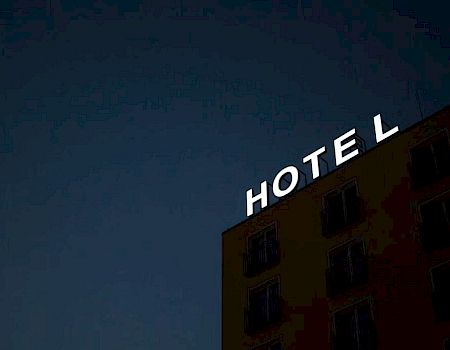 A building with the word "HOTEL" in bright lights, missing the letter "E" against a dark evening sky.