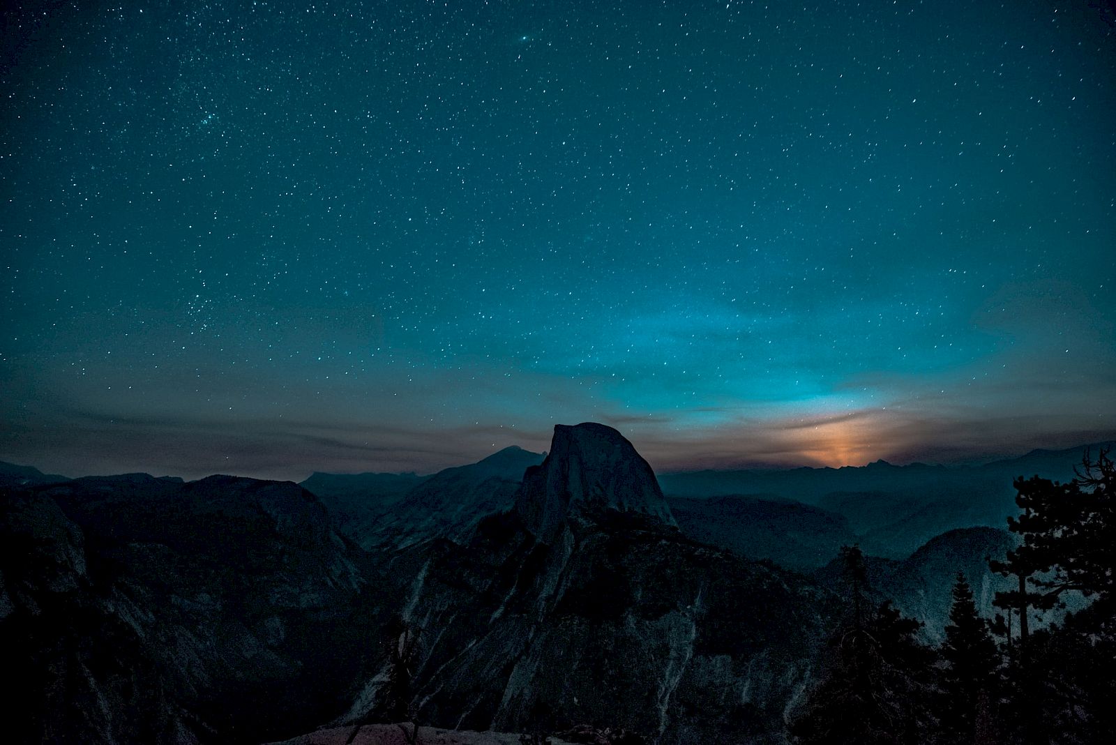 A starry night sky over a mountainous landscape with a glowing horizon, possibly a sunset or sunrise, adds a serene and mystical ambiance.