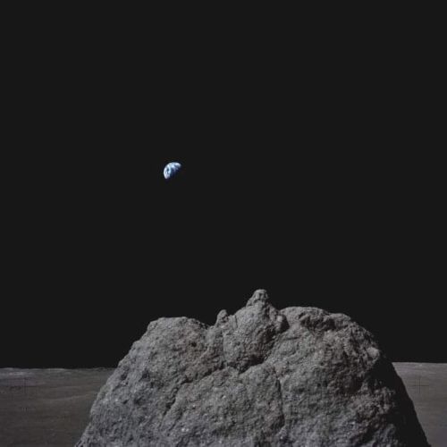 A rocky lunar surface is in the foreground, with Earth visible above it against the dark space background.