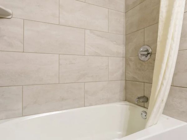 A bathroom with a white bathtub, beige tiled walls, chrome fixtures, and a shower curtain partially covering the tub.