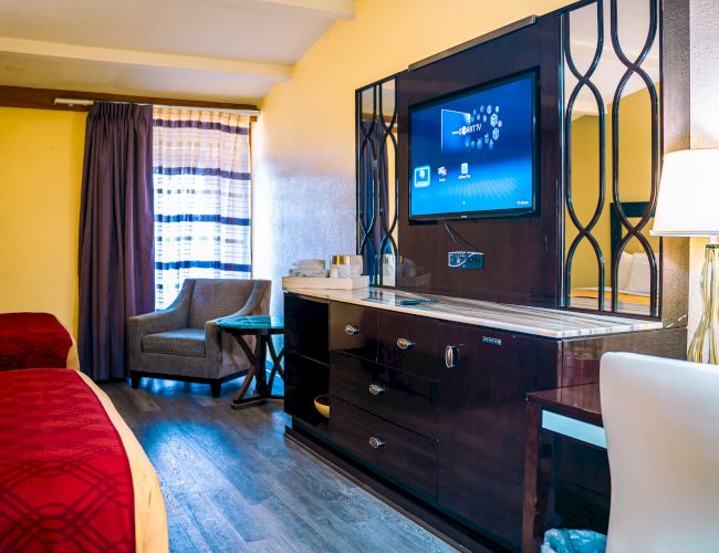 A hotel room with two beds, a TV, a chair, a lamp, and a window with curtains, featuring modern decor.
