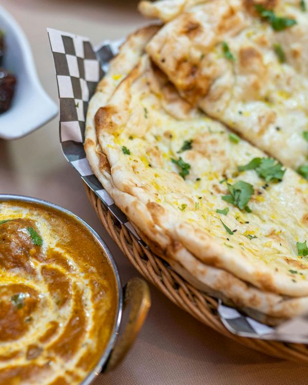 The image shows a spread of Indian cuisine: naan bread, a curry dish with meatballs, and a side of vegetables with herbs.