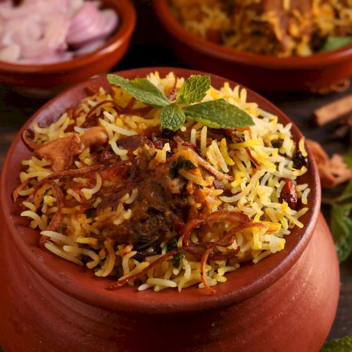 A bowl of biryani garnished with mint leaves is featured, along with a side of sliced onions in the background.