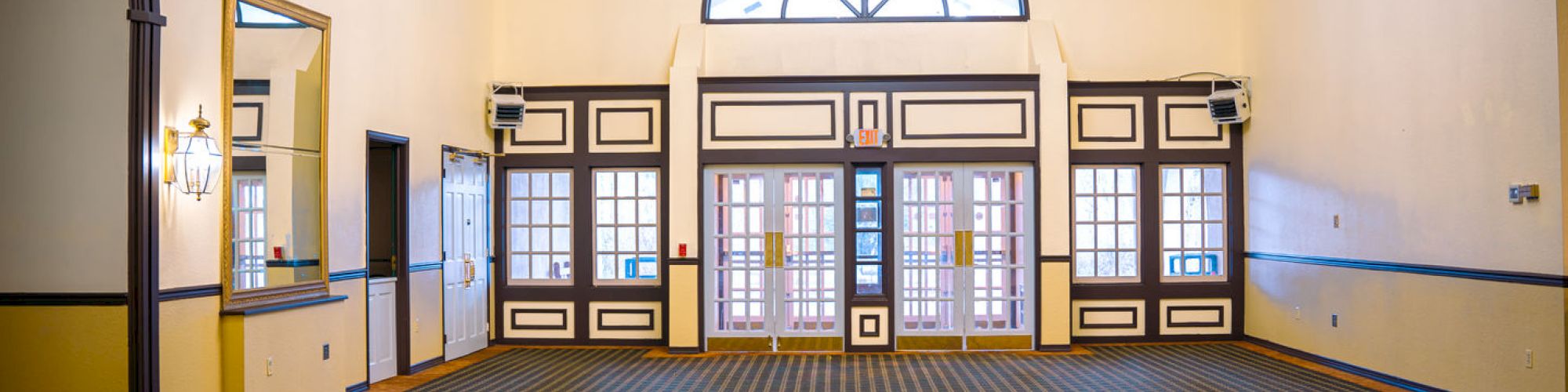 An empty room with patterned flooring, large windows, chandeliers, and vintage decor, featuring a central arched window.