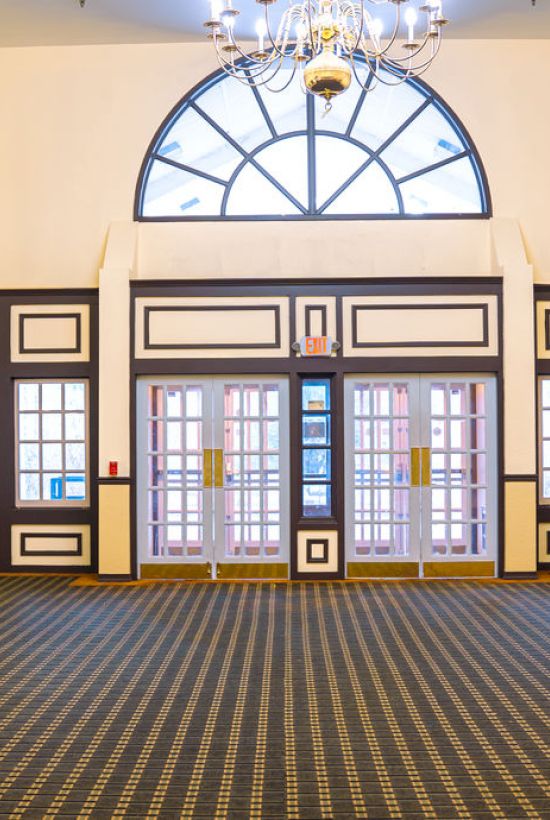 A spacious, elegantly decorated interior with large windows, patterned carpet, mirrors, and chandeliers, creating a classic and formal atmosphere.