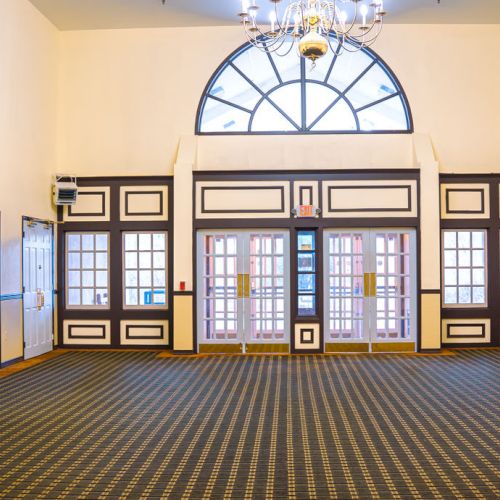 This image shows an empty, spacious room with decorative windows, carpet flooring, and elegant wall sconces.