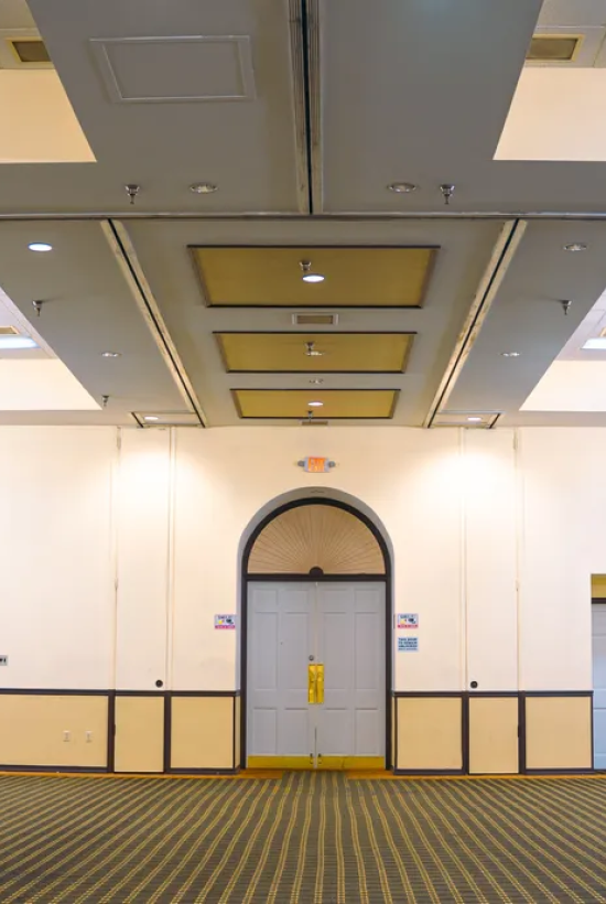 An empty banquet hall with chandeliers, carpeting, and stage lighting equipment on the right side.