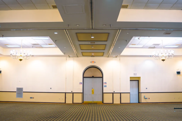 An empty, carpeted conference room with chandeliers, several doors, and lighting equipment on the side.
