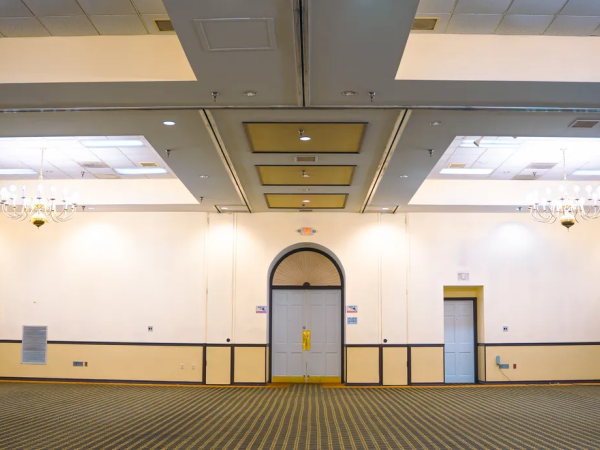 An empty, carpeted conference room with chandeliers, several doors, and lighting equipment on the side.