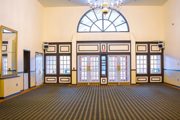 An empty, elegant room with a checkered floor, large windows, and chandeliers, exuding a classic and spacious atmosphere.