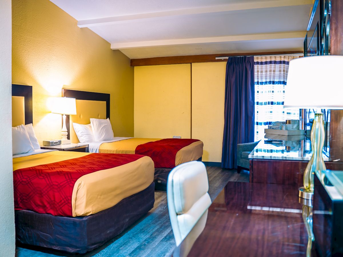 The image shows a hotel room with two beds, a desk with a chair, lamps, a TV, and curtains covering the window.