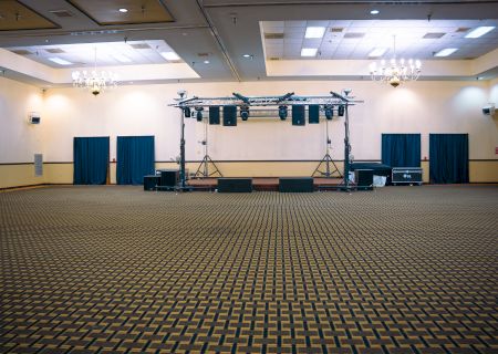 An empty event hall with patterned carpet, stage, lighting equipment, and chandelier.