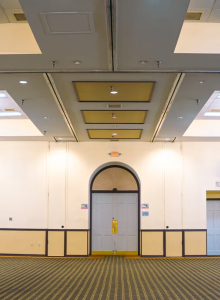 An empty event hall with chandeliers, a stage setup on the right, and multiple doors around the room.