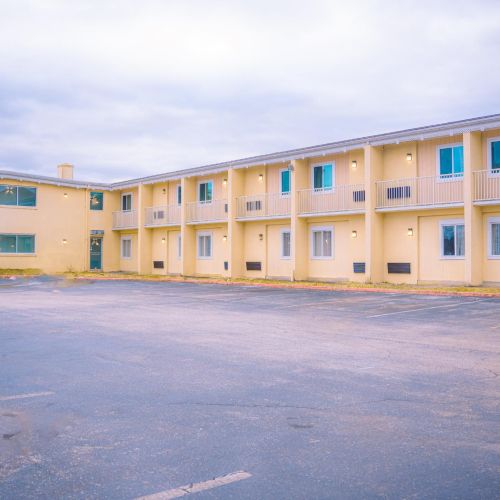 A two-story motel with a large, empty parking lot and a partly cloudy sky in the background.