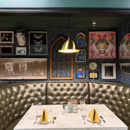A cozy restaurant booth with a marble table, yellow napkins, and eclectic framed art on dark walls under warm lighting.