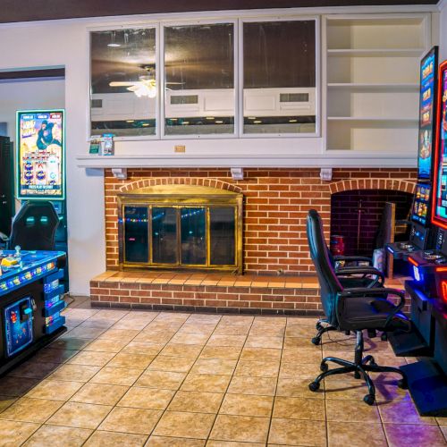 The image shows a room with arcade gaming machines, chairs, and a brick fireplace against a tiled floor.