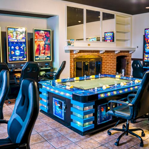 A gaming room with multiple gaming chairs, arcade game screens, and a central gaming table setup, creating an immersive play environment.
