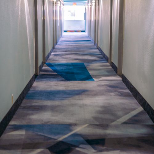 A brightly lit corridor with geometric-patterned carpet and doors on either side, leading to a bright exit at the end.