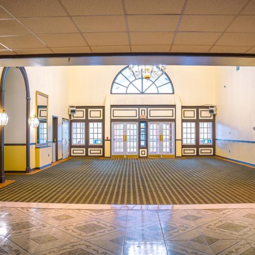 A spacious, empty room with large arched windows, checkered floor, and chandeliers, creating an elegant atmosphere.