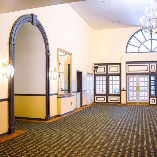 An elegant room with patterned carpet, arched doors, chandeliers, and large windows, exuding a classic and sophisticated ambience.