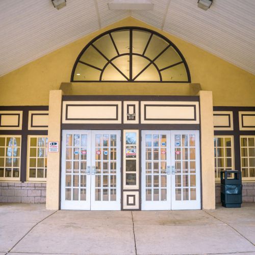 The image shows the entrance of a building with symmetrical design, large windows, two trash bins, and a semi-circular window above.