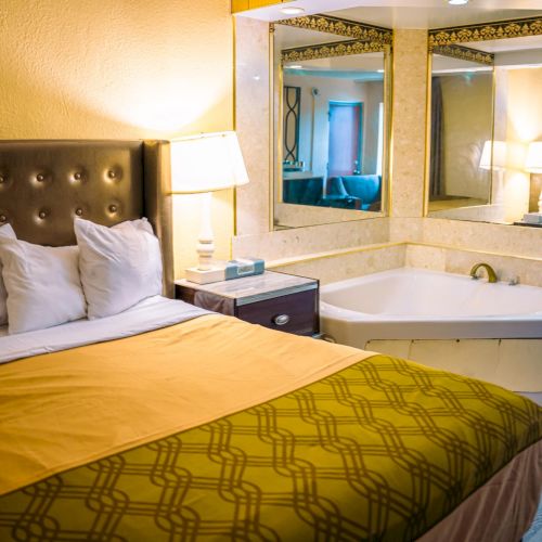 A cozy hotel room features a bed with a patterned blanket, a nightstand with a lamp, and a bathtub near mirrors.