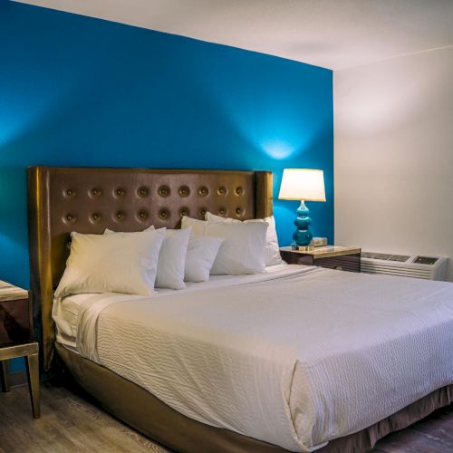 A neatly made bed with white linens and two lamps on side tables in a room with a blue accent wall and wooden flooring.