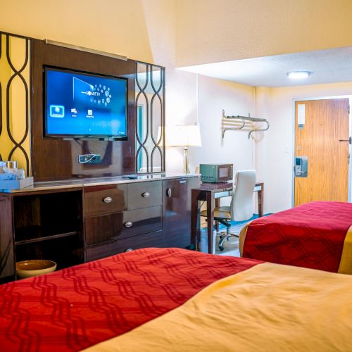 The image shows a hotel room with two beds, a TV, a desk, and an open door leading to the outside.