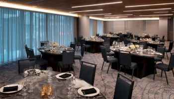 The image shows an elegantly set dining room with round tables, chairs, and decorative centerpieces, ready for an event.