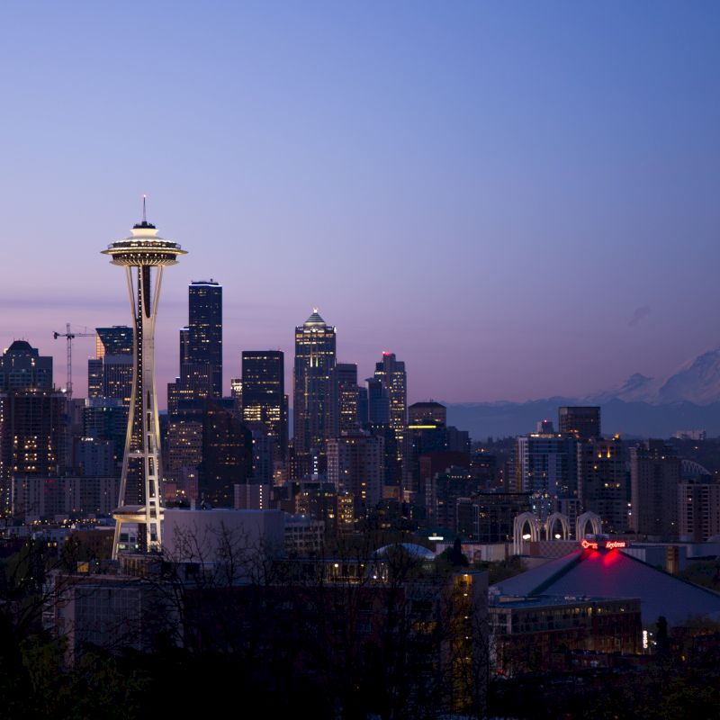 The image shows the Seattle skyline at dusk, with the Space Needle prominently featured and Mount Rainier in the background.