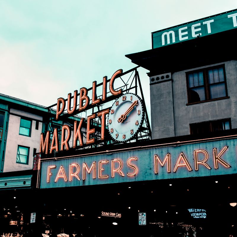 This image shows a neon sign for a "Public Market" and "Farmers Market" with a clock, likely indicating a popular market location.