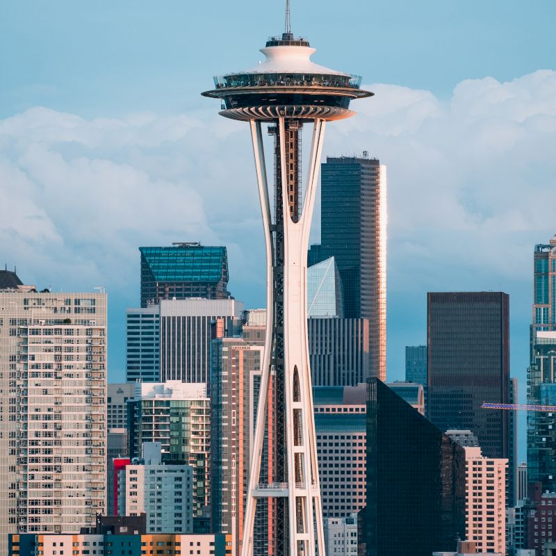 The image shows the Seattle Space Needle with a backdrop of city skyscrapers and cloudy skies.