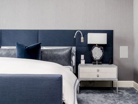A modern bedroom features a blue and white bed, a nightstand with a lamp, and minimalist decor.