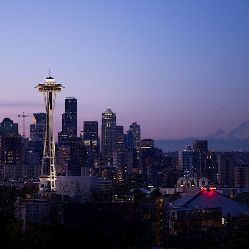Seattle skyline at dusk with the Space Needle and distant Mount Rainier against a purple-blue sky in the background.