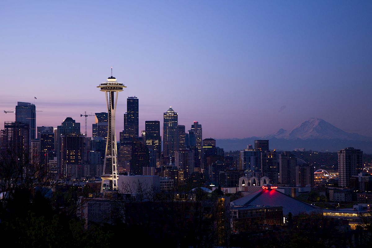 Seattle skyline at dusk with the Space Needle and Mount Rainier visible in the background, under a clear sky.