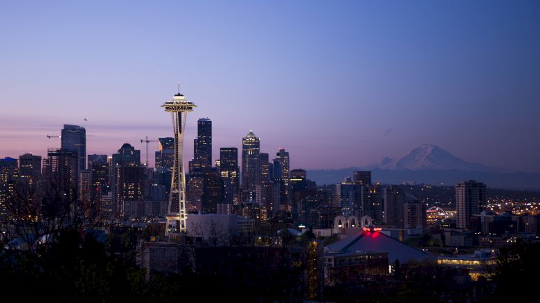 Seattle skyline at dusk with the Space Needle and Mount Rainier visible in the background, under a clear sky.