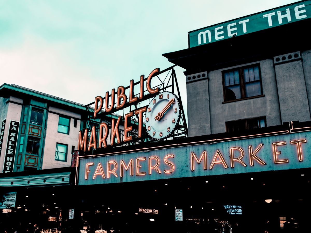 The image shows a classic neon sign for "Public Market" and "Farmers Market" with an iconic clock, likely located in an urban setting.