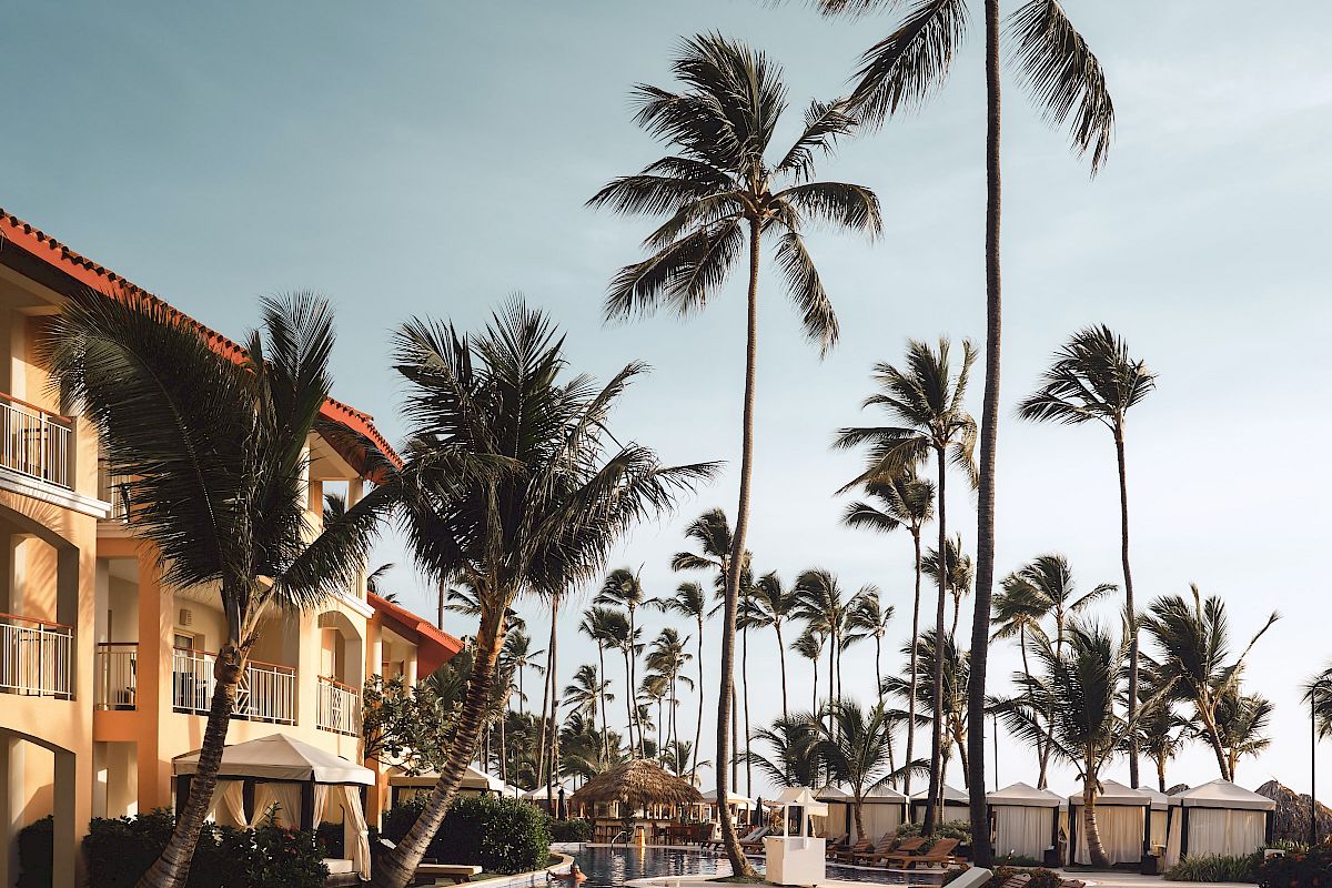 A serene poolside scene with lounge chairs, tall palm trees, and a building under a clear blue sky.
